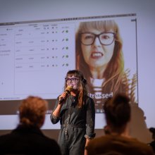 Photo of Victoria Melody holding a mic talking to an audience.