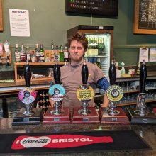 An image of a man standing behind four beer pumps.