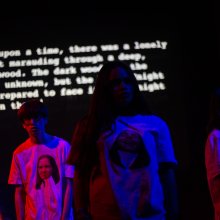 A group of people in a darkened room, illuminated by blue and pink filters.