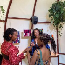 Three women chat to each other in a high ceilinged tent-like structure.
