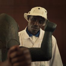 A man wearing a white bucket hat cocks his head as he looks at a masked statue.