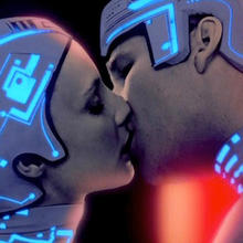 Scene from Ton - a  couple dressed in neon headgear kissing.