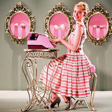 Woman dressed in pink sitting at typewriter smiling.