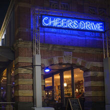 Photo of the exterior of Watershed at night with a large neon sign saying Cheers Drive, as part of Bristol Light Festival