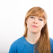Photo of a white woman with long hair, looking straight at the camera and wearing a blue jumper