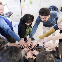 Photo of a group of adults with their hands on top of each other in the middle of a circle