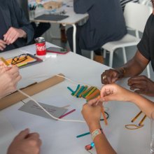 Photo of people working together around a table making things with string and lollipop sticks and more