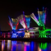 Photo of 3 cranes on Bristol harbourside at night, lit up by multi-coloured lights lights