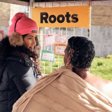 Play:Disrupt Creative High Streets Project, two people outside looking at note cards under an orange sign saying 'roots'