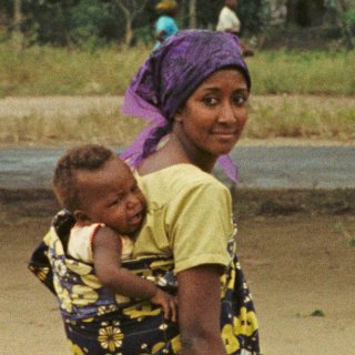 Colour photo of a women, glancing over her shoulder carrying a baby in a papoose