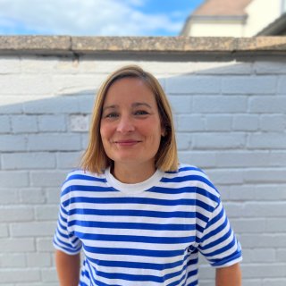 A portrait photograph of a woman looking to the camera, smiling, wearing a blue and white striped t-shirt