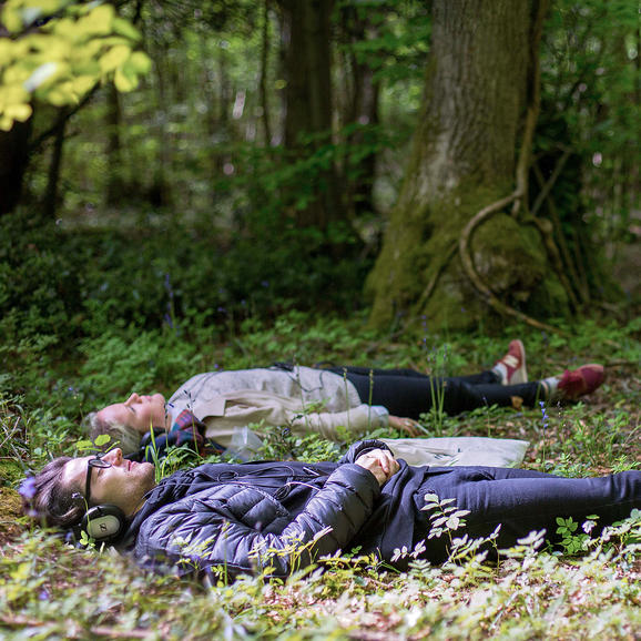 Still from Afterlife - two people lying in a wood listening to headphones