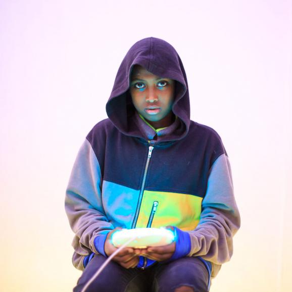 Girl in a hood sitting down holding a glowing light