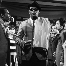 an image of a man in sunglasses standing in the middle of a crowd.