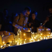 Lights and glass items are displayed on a counter, people are looking at them and interacting with them.