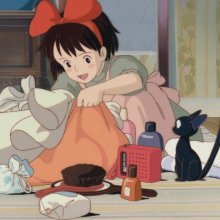 Animated girl with a red bow unpacking a bag on the floor, surrounded by toiletries and a small black cat sitting next to folded towels.