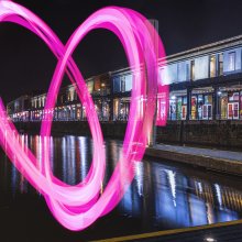 Watershed building at night, shot from the water, with a large pink heart drawn across the whole building.