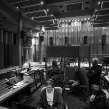 A greyscale still of a large room, filled with audio equipment. 