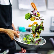 shot of chef's hand tossing a salad into a silver bowl