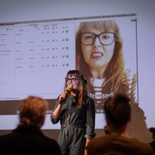 Photo of Victoria Melody holding a mic talking to an audience.