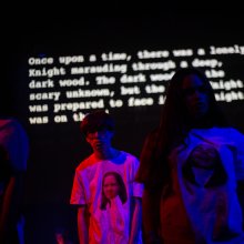 A group of people in a darkened room, illuminated by blue and pink filters.