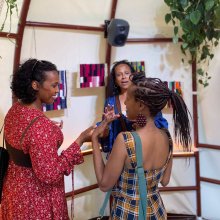 Three women chat to each other in a high ceilinged tent-like structure.