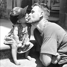 A black and white photo of the artist Andrew Kötting kissing his daughter Eden on the cheek.