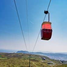 A coral coloured barrel like character sits in a cable car with a beautiful landscape behind it in Llandudno.