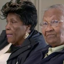Two older black women, one looking into the camera