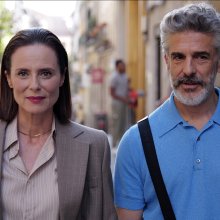 Two people wearing business casual clothes, standing outdoors on a sunny street with blurred background.