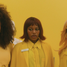 Three women with name tags, styled in yellow outfits and bold hairstyles, standing against a yellow background.