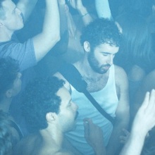 Crowded concert audience dancing and raising their hands under blue stage lighting.