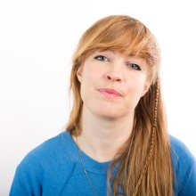 Photo of a white woman with long hair, looking straight at the camera and wearing a blue jumper