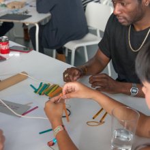 Photo of people working together around a table making things with string and lollipop sticks and more