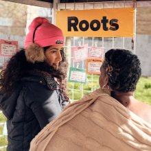 Play:Disrupt Creative High Streets Project, two people outside looking at note cards under an orange sign saying 'roots'