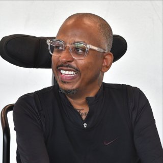 A man in a black wheelchair smiles to the side.