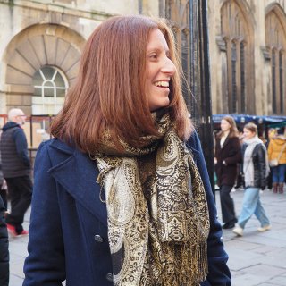 Head and body shot of Charlotte Lester, Watershed Board member, smiling, with red long hair, wearing a blue coat and a patterned scarf.