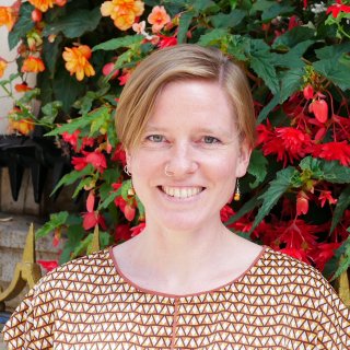 Headshot of Kate Arthurs, Watershed Board member, wearing a brown, patterned top with flowers in the background
