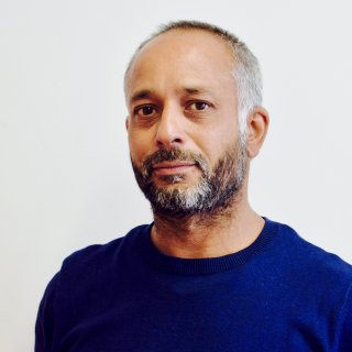 Head shot of Sidarth Sharma, Watershed Board member, with a grey beard, wearing a blue jumper.