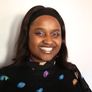 Photograph of Louise Ndibwirende wearing a black top with a colourful pattern on a plain background