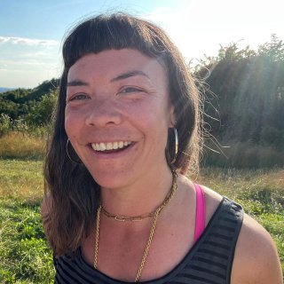 A photo of a woman called Toki Allinson standing in a field on a sunny day, smiling at the camera