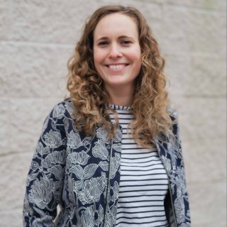 Head and shoulder shot of smiling woman standing against a white brick wall