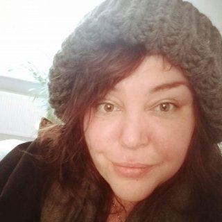 A portrait photo of a white woman looking to the camera, smiling and wearing a grey wooly hat