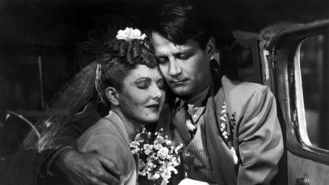 an black and white image of a couple hugging each other in a car. 