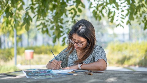 Woman seated outside painting at a table.