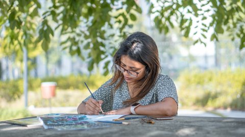 Woman seated outside painting at a table.