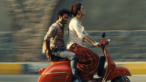 Two people ride on a red scooter, the background a blur.