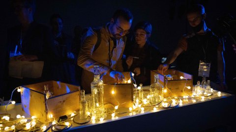 Lights and glass items are displayed on a counter, people are looking at them and interacting with them.
