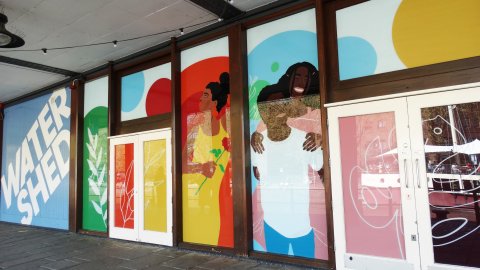 Exterior shot of Watershed with blue wood panelling displaying the Watershed logo and vinyls of smiling people covering the windows.