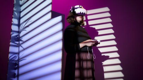 A woman stands in a VR Headset experiencing Impulse: Playing with Reality.